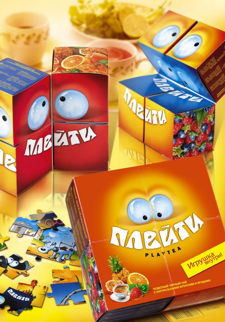 Красочная упаковка Плейти (Play Tea) от Soldis с мультяшными глазами, с изображениями фруктов и пазлами. Коробки показаны открытыми и закрытыми, окруженными чашками чая и чайником на желтой поверхности.