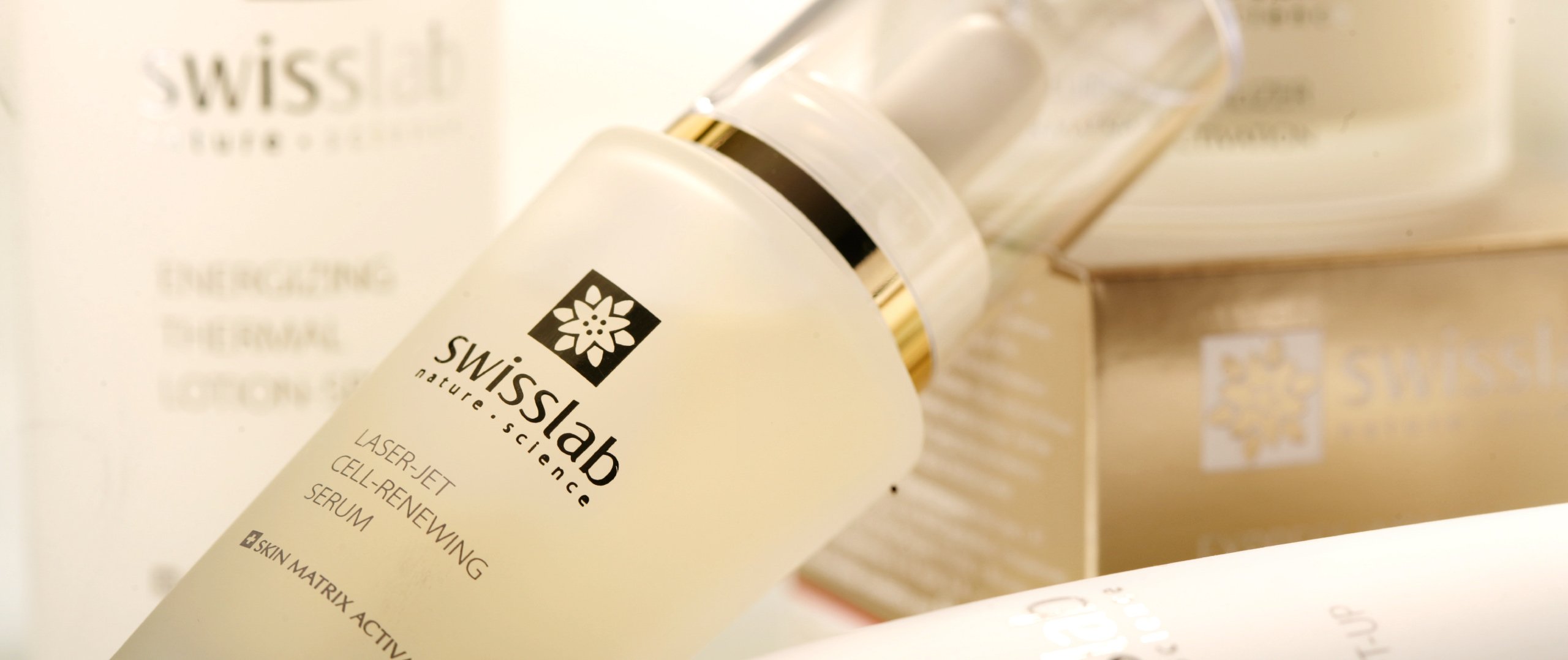 Крупным планом флакончик средства по уходу за кожей Swisslab с надписью Laser Jet Cell-Renewing Serum и крышкой-пипеткой, расположенный среди других средств по уходу за кожей под брендом Swisslab в дизайне от Soldis.
