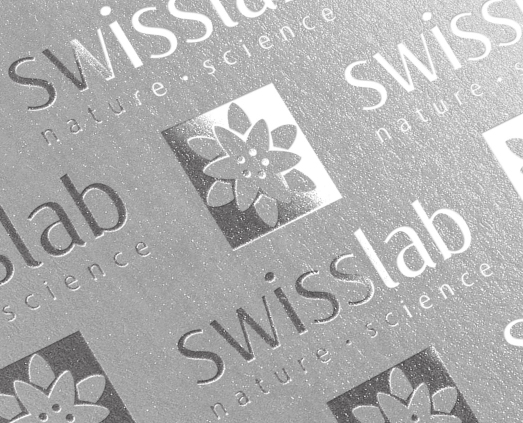 Упаковка из тисненого серебра с логотипом Swisslab, стилизованным цветком в квадрате и надписью в дизайне от Soldis